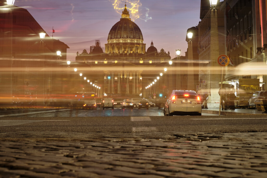 Kapitel 12 - Wenn es Abend wird, Rom, Abend, Dämmerung, Petersdom im Hintergrund, lange Straße und verwischte Autolichter